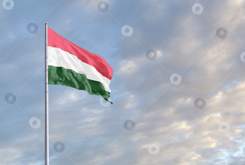 Скачать Развевающийся венгерский флаг на фоне голубого неба с облаками и пустым пространством для текста. Место для текста фотосток Ozero