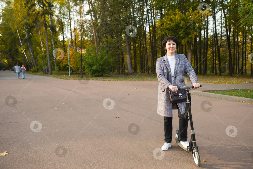 Скачать Сеньора за 50 на скутере в повседневной одежде наслаждается жизнью на прогулке в парке. Активный образ жизни в среднем возрасте, занятия спортом. Пространство для копирования фотосток Ozero