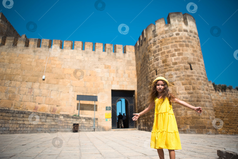 Скачать Девушка-туристка в желтой шляпке и сарафане прогуливается по каменной улице старого города с крепостью. Тур по достопримечательностям. Ребенок заблудился, разыскивая родителей фотосток Ozero
