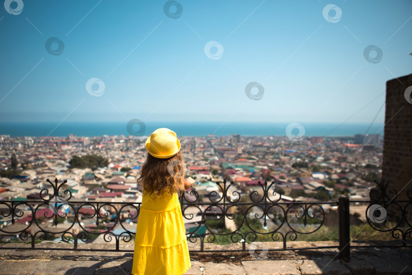 Скачать Девушка-туристка в желтой шляпке и сарафане смотрит с высоты на смотровую площадку на город. Тур по достопримечательностям. Ребенок заблудился, разыскивая родителей фотосток Ozero