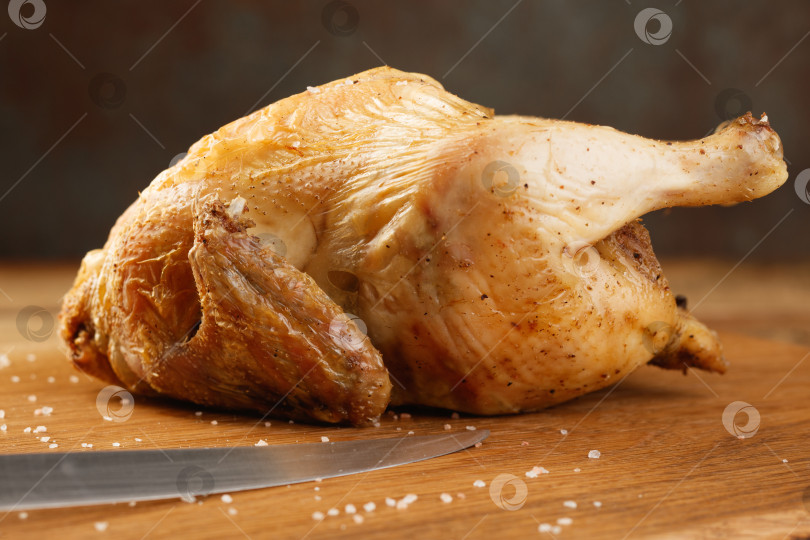 Скачать Запеченная целиком курица и нож на деревянной доске. фотосток Ozero