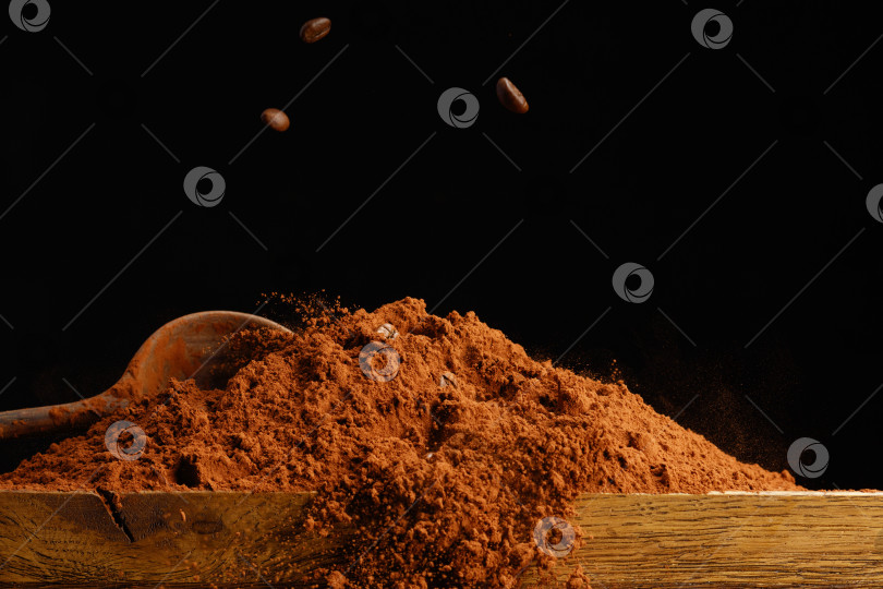 Скачать Падающие кофейные зерна на кучку шоколадной пудры на деревянном столе. фотосток Ozero