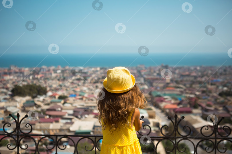 Скачать Девушка-туристка в желтой шляпке и сарафане смотрит с высоты на смотровую площадку на город. Тур по достопримечательностям. Ребенок заблудился, разыскивая родителей фотосток Ozero