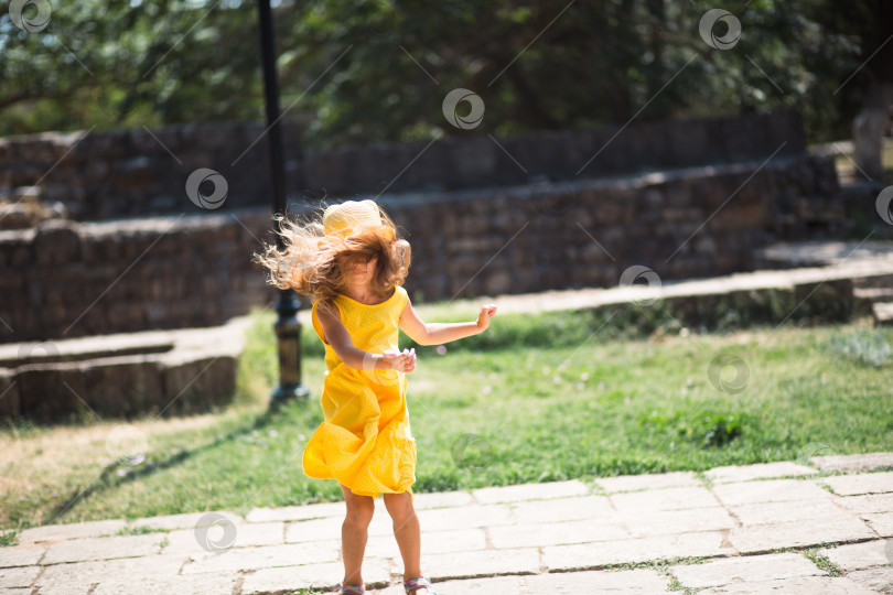 Скачать Девушка-туристка в желтой шляпке и сарафане танцует по каменной улице старого города с крепостью. Тур по достопримечательностям. фотосток Ozero