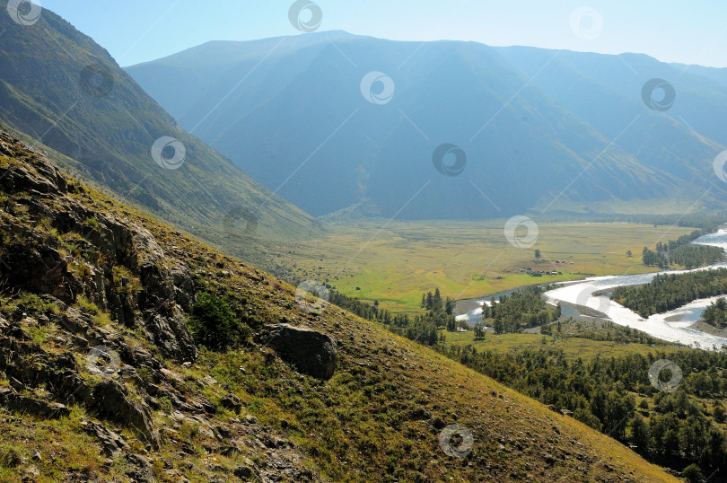 Скачать Вид с вершины на живописную долину в горах, залитую теплым солнечным светом, и русло извилистой реки. фотосток Ozero
