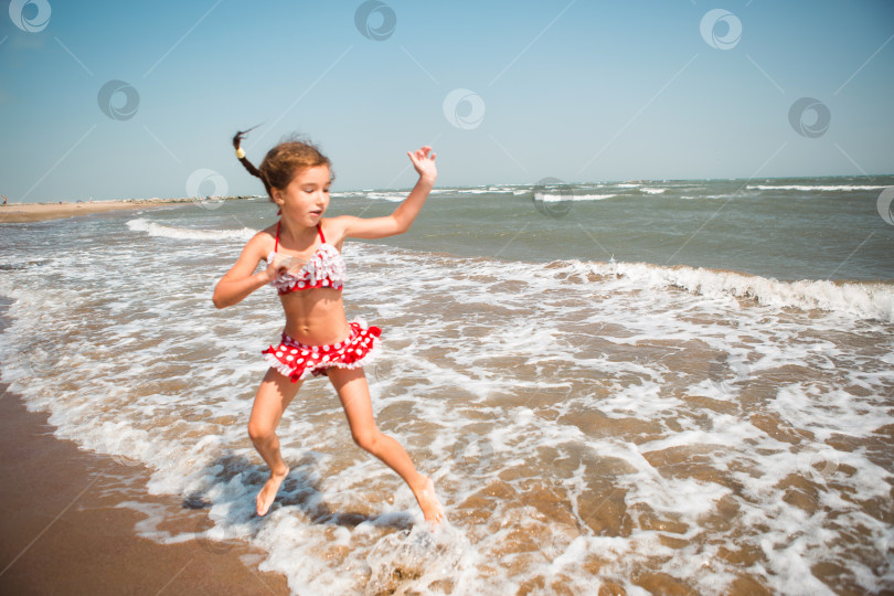 Скачать Маленькая девочка в красном купальнике играет на пляже с морской волной - прыгает, бегает, веселится. Плавание, путешествия, игры с водой фотосток Ozero