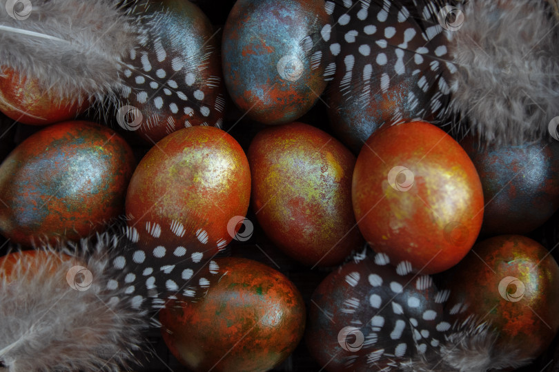 Скачать Фон из раскрашенных коричневых, золотых, синих и серебряных пасхальных яиц с перьями крупным планом сверху фотосток Ozero