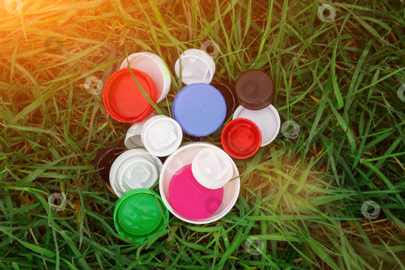 Скачать Разноцветные крышки от пластиковых бутылок на зеленой траве. Волонтерская благотворительная акция "Добрые крышки" в помощь детям-сиротам. фотосток Ozero