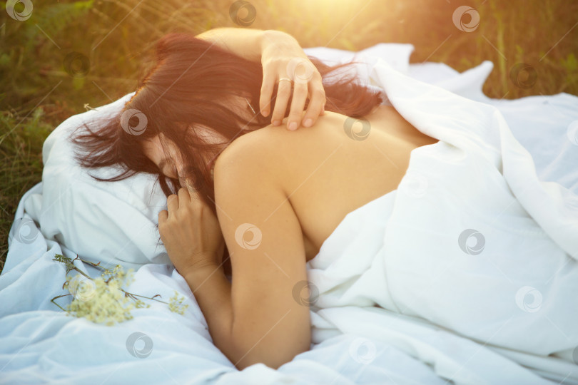 Скачать Молодая женщина лежит на своем постельном белье в траве с обнаженными плечами. Нежность, доброе утро, забота о себе, сладкий сон на свежем воздухе. фотосток Ozero