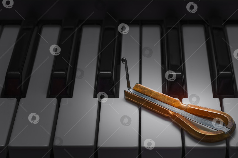 Скачать Этническая еврейская арфа лежит на клавишах пианино. Два музыкальных инструмента крупным планом. Концепция народных мотивов в современной музыке. фотосток Ozero