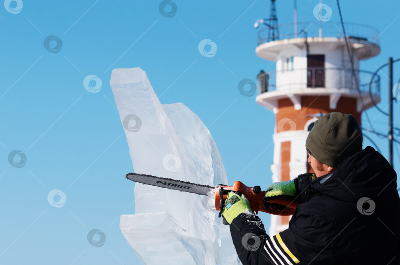 Скачать Скульптор вырезает фигуру из ледяной глыбы с помощью электрической бензопилы. Ледяная пыль в воздухе. фотосток Ozero