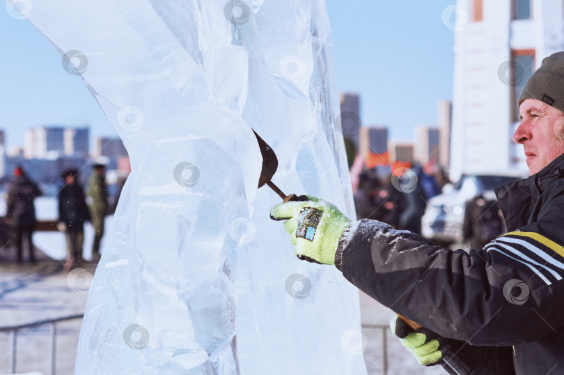 Скачать Скульптор вырезает ледяную фигуру из ледяной глыбы зубилом в солнечный зимний день. фотосток Ozero
