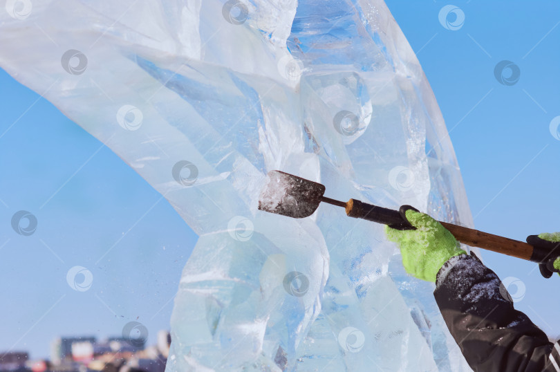 Скачать Скульптор с помощью резца вырезает ледяную фигуру из ледяной глыбы солнечным зимним днем. фотосток Ozero