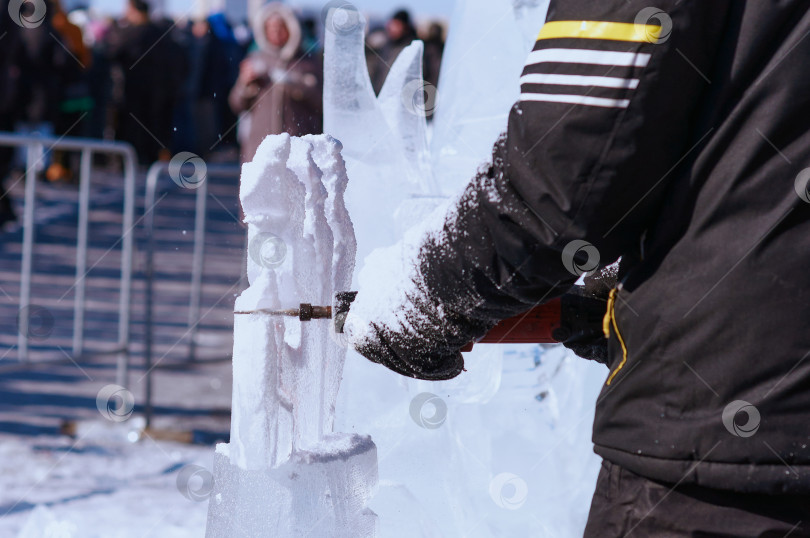 Скачать Резьба по льду крупным планом. Скульптор режет лед электроинструментом. Ледяная пыль и мусор в воздухе. Зимний фестиваль ледяных скульптур. фотосток Ozero