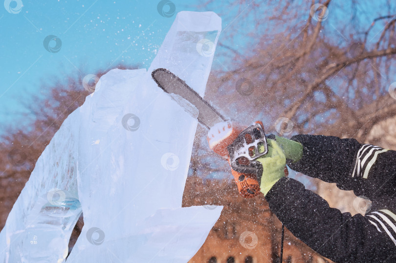 Скачать Электроинструмент в руках скульптора высекает ледяную фигуру на фоне голубого неба. фотосток Ozero