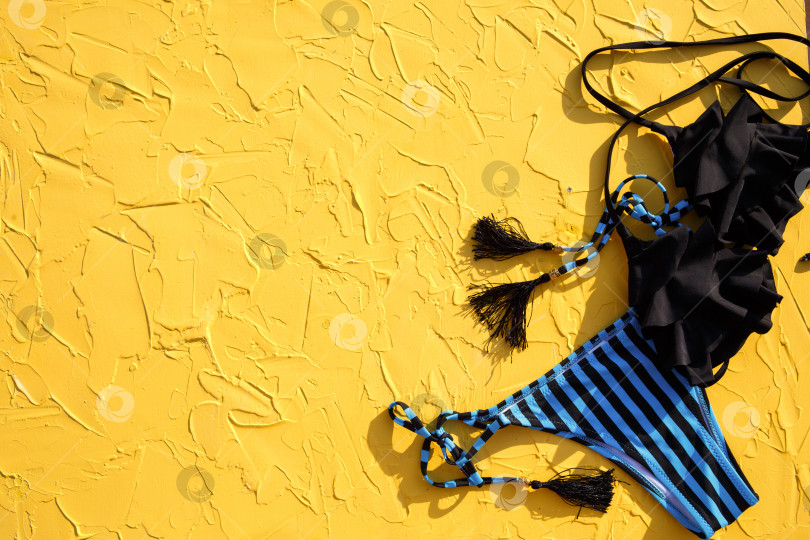 Скачать Синий с черными полосками женский купальник и солнцезащитные очки на желтом фоне. Концепция пляжного отдыха, поездки на море, аксессуары для плавания, защита от ультрафиолета, загар. Копировальное пространство. Плоский лист фотосток Ozero