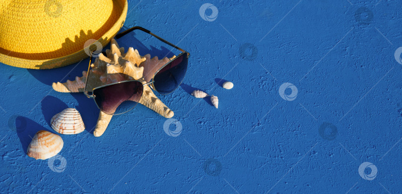 Скачать Рамка с пляжными аксессуарами на морскую тематику: желтая соломенная шляпа, солнцезащитные очки, морская звезда и ракушки на синем фоне. Концепция отпуска, морская прогулка, защита от ультрафиолета, плавание. Пространство для копирования. Плоский лист фотосток Ozero