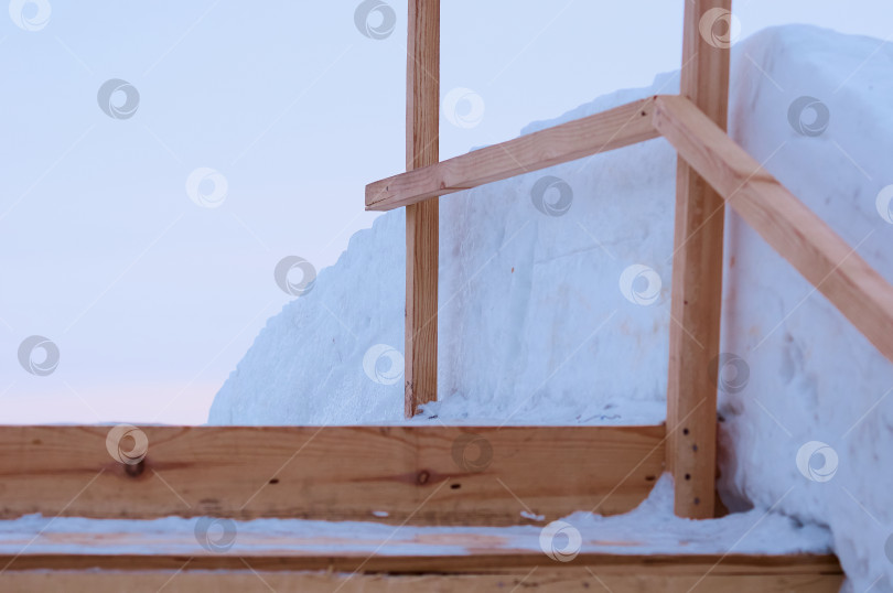 Скачать Заснеженные ступени деревянной лестницы, ведущей к ледяной горке. Временное зимнее сооружение из свежих досок. фотосток Ozero