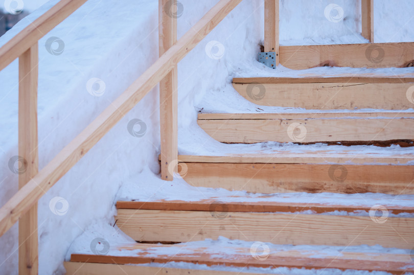 Скачать Заснеженные ступени деревянной лестницы, ведущей к ледяной горке. Временное зимнее сооружение из свежих досок. Избирательный фокус фотосток Ozero