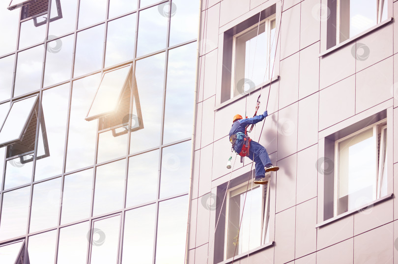 Скачать Промышленный альпинизм. Мойщик окон работает на фасаде высотного офисного здания. фотосток Ozero