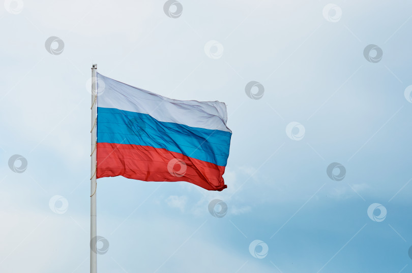 Скачать Большой российский флаг крупным планом на фоне облачного неба. Государственный символ Российской Федерации на ветру фотосток Ozero