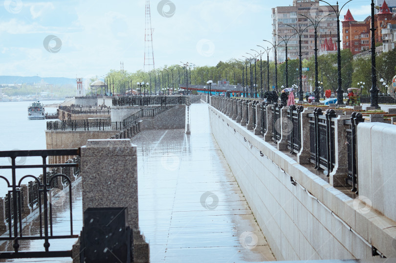 Скачать Летний дождь в солнечную погоду на набережной реки. Капли воды в воздухе. Перила забора на переднем плане. фотосток Ozero