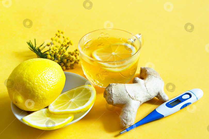 Скачать Целебный чай в чашке, имбирь, лимон, акация - укрепляют иммунитет в холодное время года, термометр - категорически. Витаминный напиток для здоровья и ингредиенты на желтом фоне. фотосток Ozero