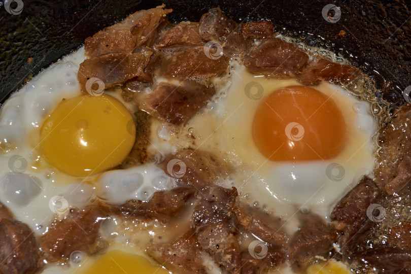 Скачать Кусочки мяса и куриные яйца обжаривают на сковороде. фотосток Ozero