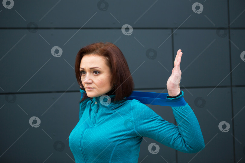 Скачать Женщина тренируется с фитнес-резинкой на городской улице. Укрепление рук с помощью эспандера и утяжелителя. Фитнес, активный здоровый образ жизни, спорт на открытом воздухе фотосток Ozero