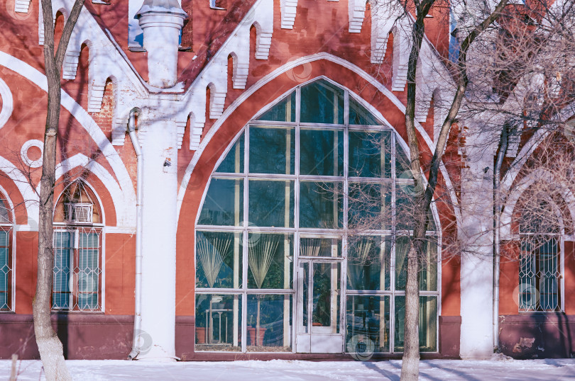 Скачать Facade of an old red brick building. Arched windows and white columns. Texture of frozen plants. Winter architectural landscape. фотосток Ozero