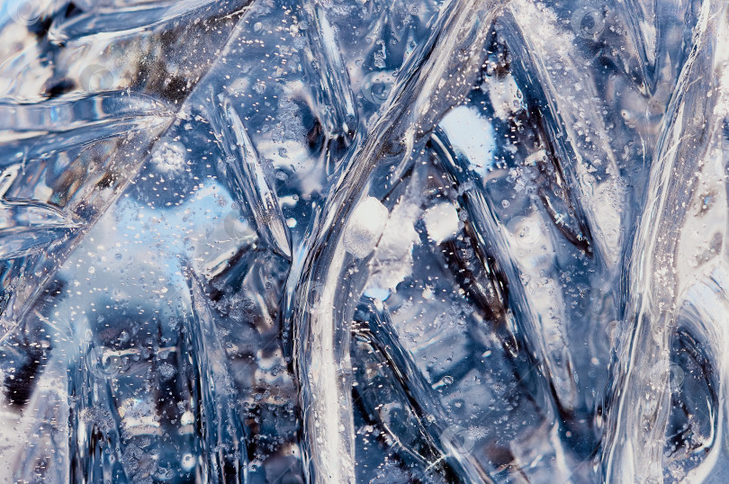 Скачать Bubbles and cracks inside natural ice. A fragment of a festive ice figure before Christmas and New Year. Optical phenomena. Abstract background. Close up. Selective focus. фотосток Ozero