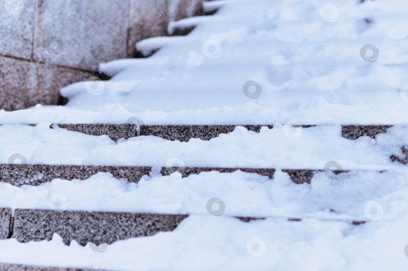 Скачать The steps of the granite stairs are covered with snow during a snowfall. Descent to the river on the city embankment. Cold day. No people фотосток Ozero