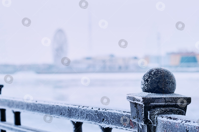 Скачать White frost on the black metal railings of the Amur river embankment on a winter morning. Ferris wheel silhouette in blur in the background. selective focus фотосток Ozero