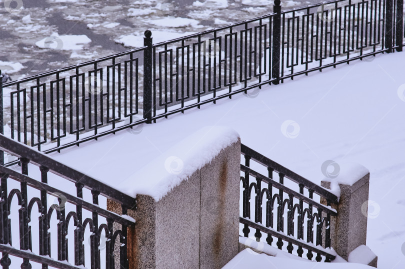 Скачать Snowfall on the embankment of the Amur River during ice drift. Black metal railings. Stair railing covered with snow. фотосток Ozero