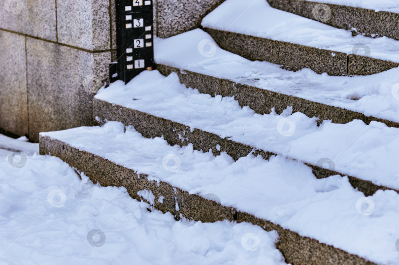 Скачать The steps of the granite stairs are covered with snow during a snowfall. Descent to the river on the city embankment. фотосток Ozero