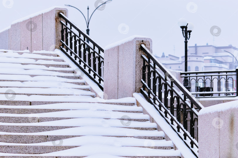 Скачать The steps of the granite stairs are covered with snow during a snowfall. фотосток Ozero