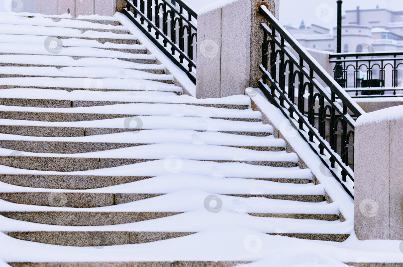 Скачать The steps of the granite stairs are covered with snow during a snowfall. Descent to the river on the city embankment. фотосток Ozero