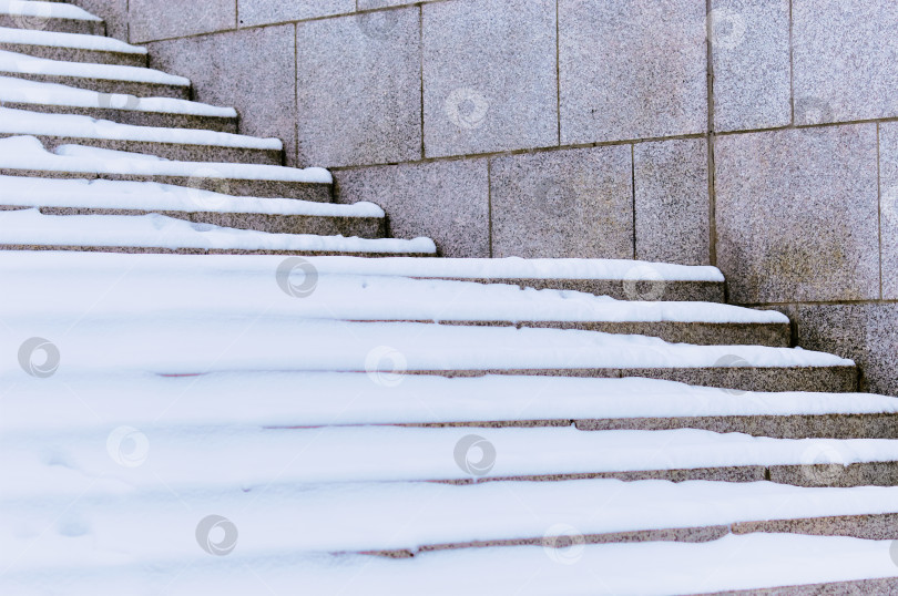 Скачать The steps of the granite stairs are covered with snow during a snowfall. Descent to the river on the city embankment. Cold day. No people фотосток Ozero
