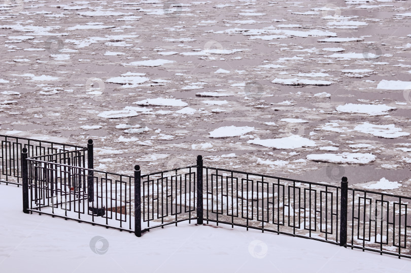 Скачать Ice drift on the river in winter. Black fence on a snowy embankment. фотосток Ozero