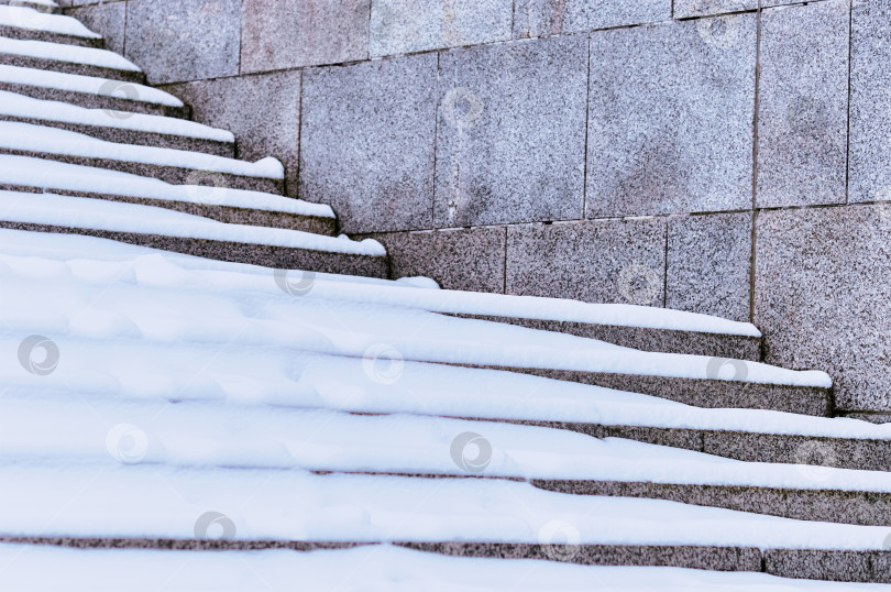 Скачать The steps of the granite stairs are covered with snow during a snowfall. Descent to the river on the city embankment. Cold day. No people фотосток Ozero