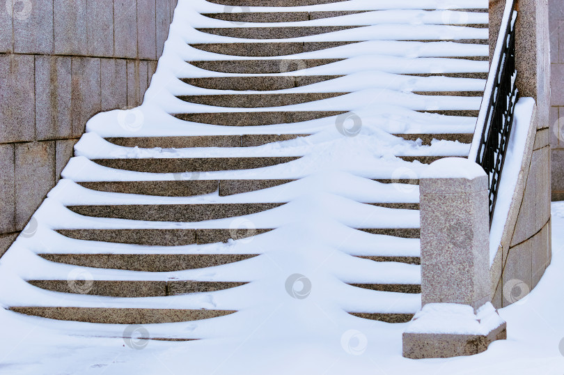 Скачать The steps of the granite stairs are covered with snow during a snowfall. Descent to the river on the city embankment. фотосток Ozero