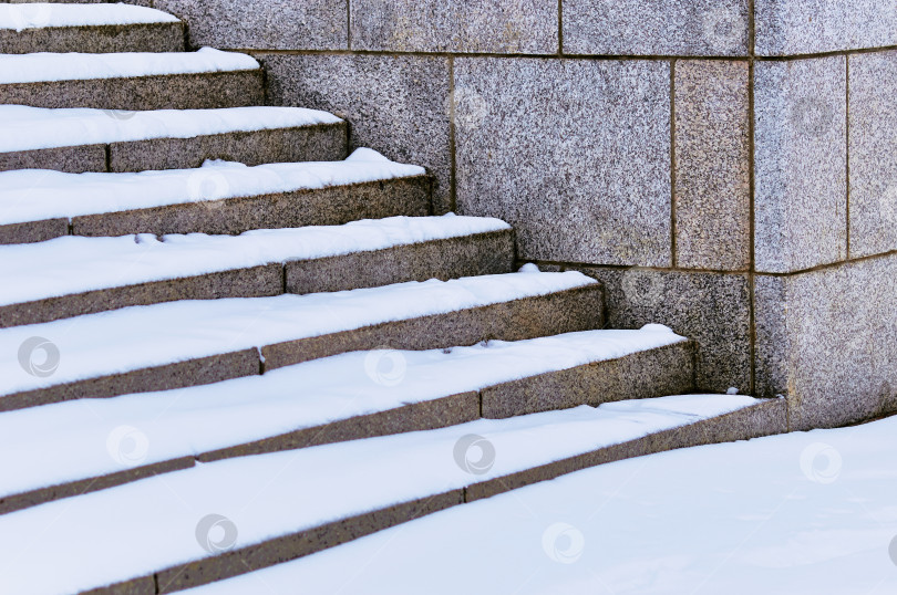 Скачать The steps of the granite stairs are covered with snow during a snowfall. Descent to the river on the city embankment. Cold day. No people фотосток Ozero