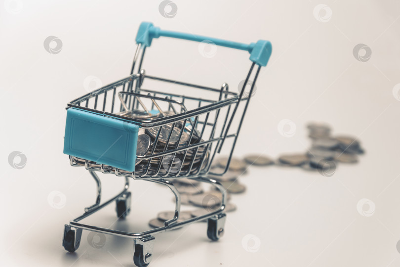 Скачать Supermarket trolley with scattered coins on a white background. фотосток Ozero