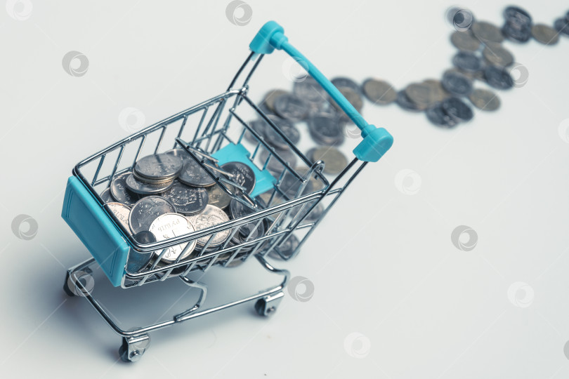 Скачать Supermarket trolley with scattered coins on a white background. фотосток Ozero
