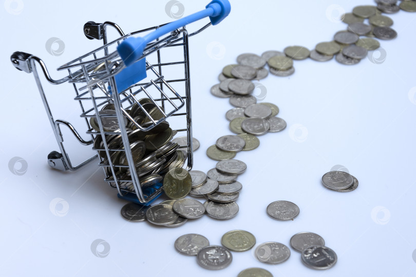 Скачать Supermarket trolley with scattered coins on a white background. фотосток Ozero