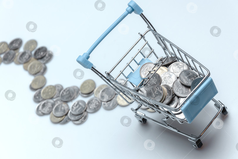 Скачать Supermarket trolley with scattered coins on a white background. фотосток Ozero