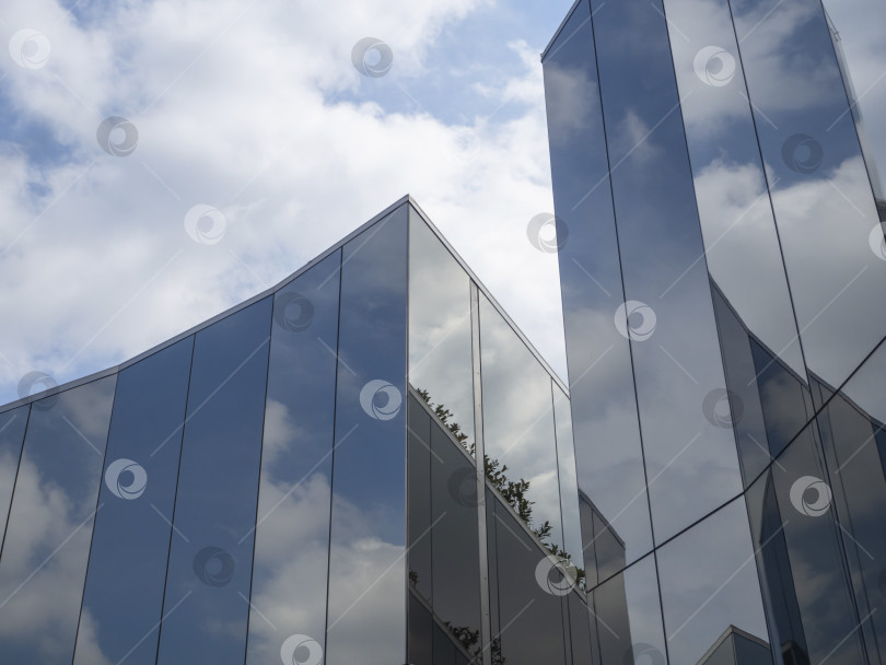 Скачать Blue sky with clouds and its reflection in modern glass architecture. Geometric towers covered with a reflective surface. White fluffy clouds. фотосток Ozero