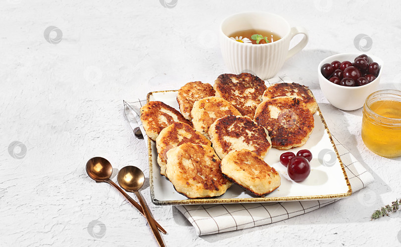 Скачать Fritters with cherries, honey and chamomile tea on a light background. The concept of healthy and natural food. Healthy breakfast with ingredients, food for kids. selective focus, flat lay, top view фотосток Ozero