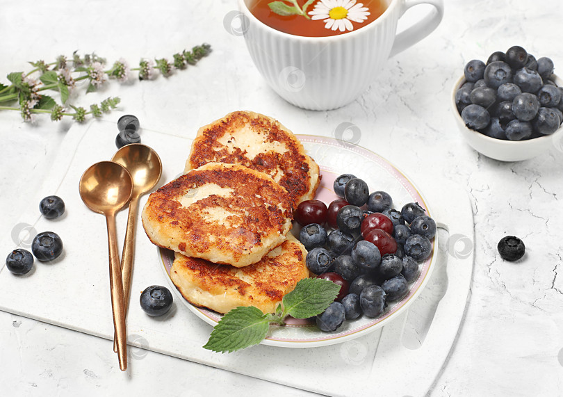 Скачать Fritters with blueberries, honey and chamomile tea on a light background. The concept of healthy and natural food. Healthy breakfast with ingredients, food for kids. selective focus, flat lay, top view фотосток Ozero