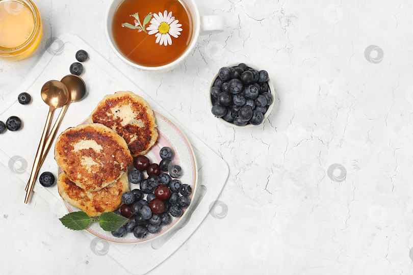 Скачать Fritters with blueberries, honey and chamomile tea on a light background. The concept of healthy and natural food. Healthy breakfast with ingredients, food for kids. selective focus, flat lay, top view фотосток Ozero